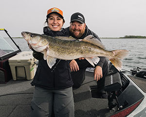 Smiling woman holding a large fish on a boat with a man behind her