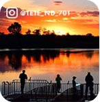 Orange sunset behind a body of water with silhouettes of people looking at it