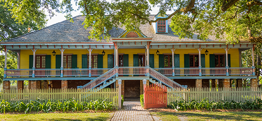 yellow house with green shutters, and large wrap around porch. 