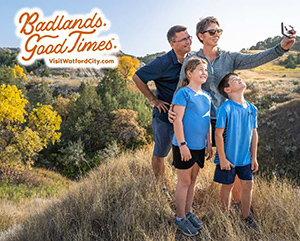 A family of four taking a selfie in a grassy landscape, with overlay text reading: Badlands. Good Times. VisitWatfordCity.com