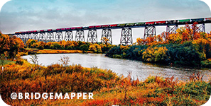 A bridge surrounded by vibrant red fall foliage, with overlay text that reads @bridgemapper