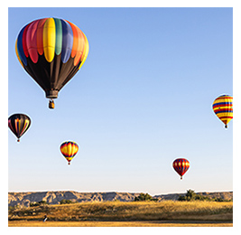 Colorful hot-air balloons in the air of a blue sky, over a grassy landscape