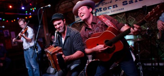 Two men perform music live, one playing the accordion and the other playing guitar.