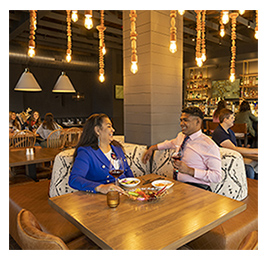 A woman in a blue jacket and a man sitting at a table in a restaurant enjoying a meal and smiling at each other