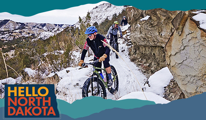 A man riding a fat-tire bike on a snowy, rocky trail, with overlay text that reads Hello North Dakota