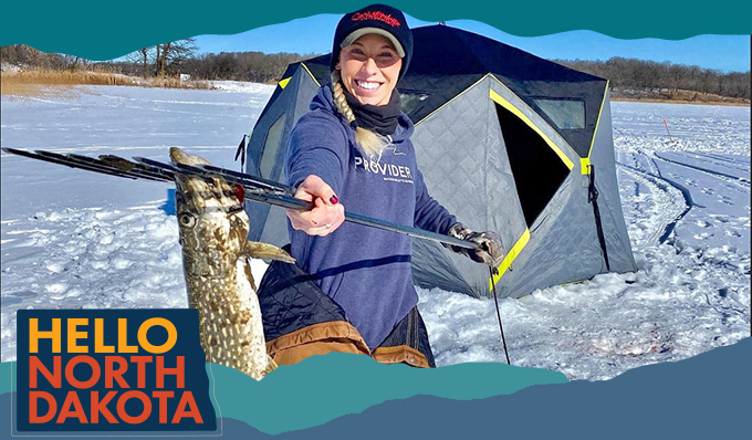 Smiling woman holding a spear with a caught fish on it in a snowy landscape, with overlay text that reads Hello North Dakota