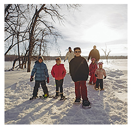 Family of adults and children snowshoeing through the outdoors