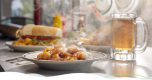 A steaming plate of shrimp étouffée is placed beside a cold mug of beer and a shrimp po'boy.