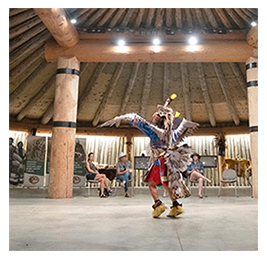 An Indigenous person performing while wearing a traditional outfit with feathers and other adornments