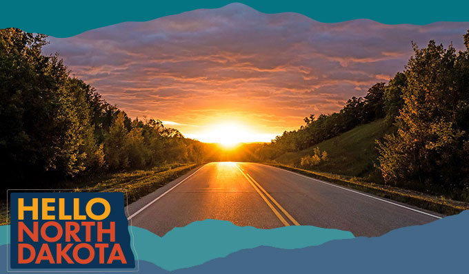 View down an empty road lined with trees and a sunset in the distance, with overlay text that reads Hello North Dakota