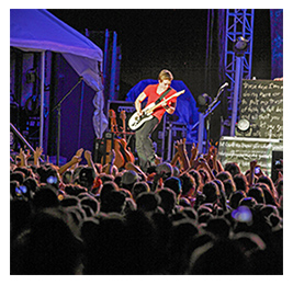Man playing a guitar on stage in front of a large crowd
