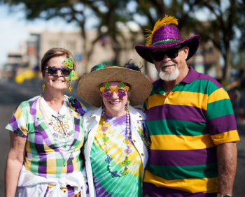Two women and a man wearing mardi gras shirts and accessories smiling.