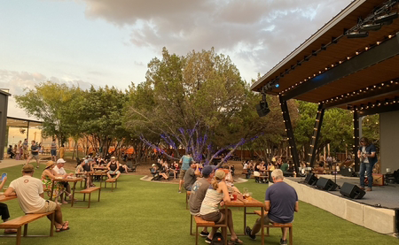 People sit at picnic tables near an outdoor stage listening to performers at Meanwhile Brewing in Austin, Texas