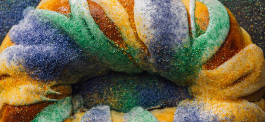 A close-up view of a the traditional purple, green and gold sugar and white icing on a king cake.