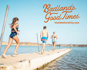 Three people running down a concrete pier towards a lake, with overlay text that reads: Badlands. Good Times. VisitWatfordCity.com