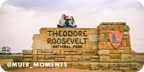 Woman and two children sitting on top of a sign made out of stones that reads 