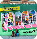 A woman and a dog posing in front of a colorful mural that reads 