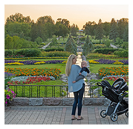Woman holding a baby while looking at a view of colorful flowers and plants in a garden