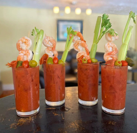 Four Bloody Mary cocktails with shrimp, celery and olives on top. 
