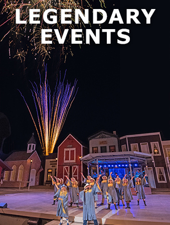 Group of people performing on a stage in front of historical-looking buildings, with fireworks in the background and overlay text that reads: Legendary Events