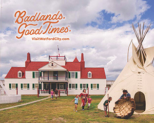 A white building with a red roof and a woman and children running in front of it toward a teepee, with overlay text that reads: Badlands. Good Times. VisitWatfordCity.com
