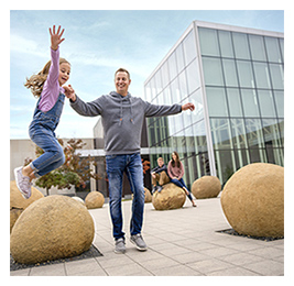Man with a young girl jumping off rocks outside of a museum