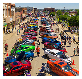 Aerial shot of lots of colorful cars lined up on a small-town street for a car show and people walking among them