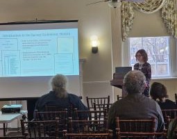 One of several speakers at the 2025 Delmarva Archaeology and History Symposium speak about an area project in front of several attendees.	