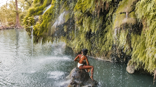 A woman perched on a rock in the middle of Krause Springs swimming hole in Spicewood, Texas