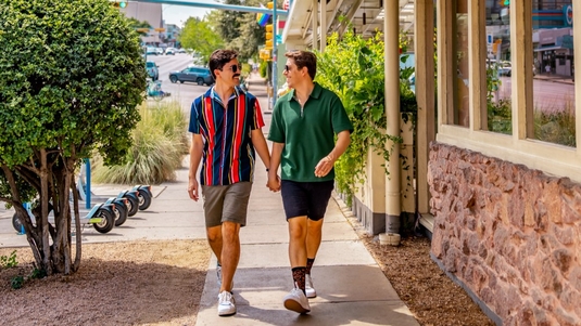 Two men hold hands while walking on a sidewalk in Austin, Texas