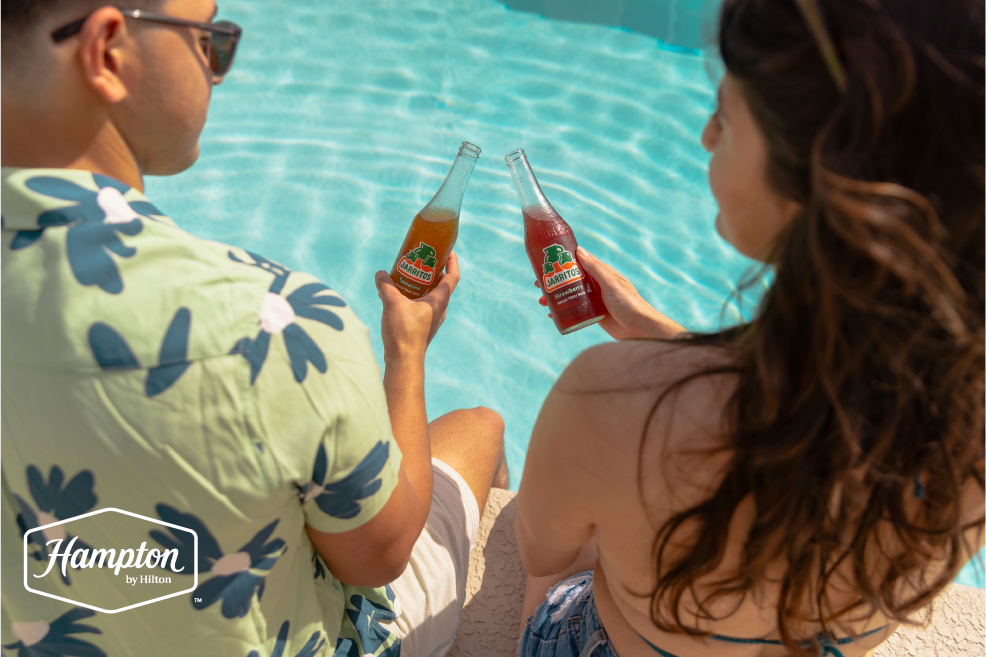 Two people sit at the edge of the pool at Hampton East Austin in Austin, Texas