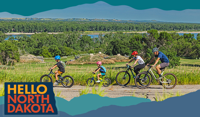 Family of two adults and two children riding bikes near trees and a body of water, with overlay text that reads: Hello North Dakota