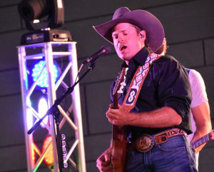 Man wearing a cowboy hat while playing a guitar on stage and singing into a microphone