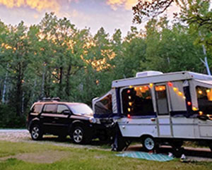 SUV and a camper trailer set up and surrounded by green trees