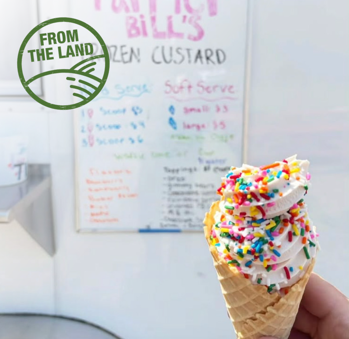 Ice cream cone full of vanilla ice cream and colorful sprinkles in front of a hand written sign. 
