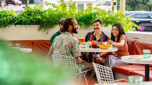 Four smiling people eat a meal on an outdoor patio along South Congress Avenue