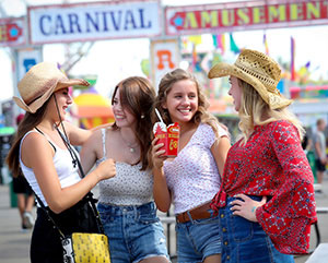 Four smiling women at a fair with signs reading 