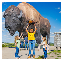Three young girls standing outside in front of a large statue of a bison