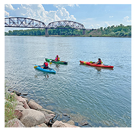 Three people in kayaks on a river with a bridge in the background