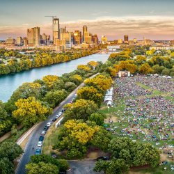 Aerial view of a crowd at a music festival in Zilker Park with the Austin skyline in the background