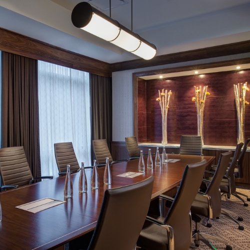 A meeting room at JW Marriott Austin set up as a boardroom with a long table, glass water bottles and chairs 
