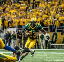football player carrying ball in a green and yellow uniform 