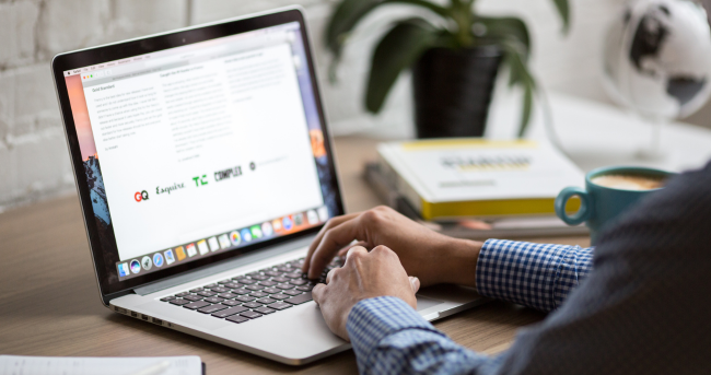 Someone at a laptop computer with open files on desk surrounding it.