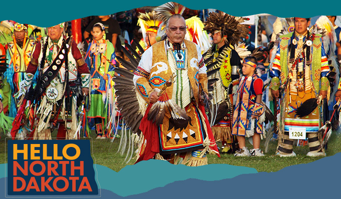 A Native American man surrounded by people with everyone wearing colorful ceremonial clothing, with overlay text that reads: Hello North Dakota