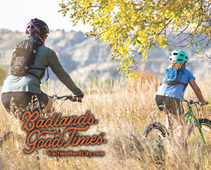 Two people riding bikes through a tall meadow, with overlay text that reads: Badlands. Good Times. VisitWatfordCity.com