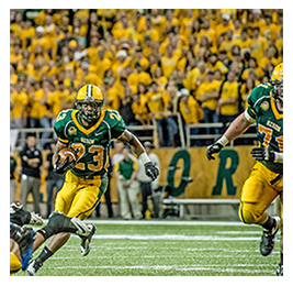 Player during a football game running with the ball with a crowd dressed in yellow behind him