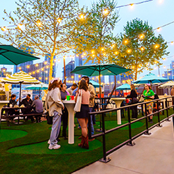 People congregate outdoors at high-top tables on the mini golf course at Holey Moley