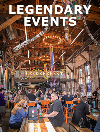People sitting at picnic tables in a venue with tall wooden ceilings with a sign that reads 