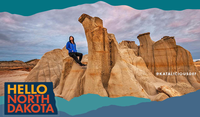 Woman sitting on tall, tan rock formations, with overlay text that reads: Hello North Dakota and @kataliciousdef