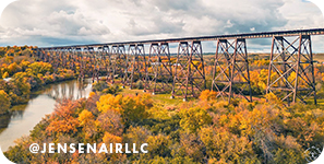 Bridge spanning over a river surrounded by colorful gold and orange trees, with overlay text that reads: @jensenairllc